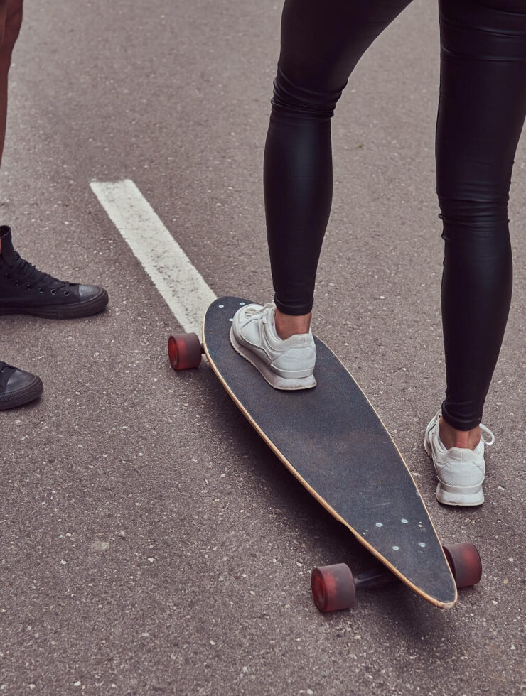 Leisure and sports concept - close-up of teenage couple feet with a longboard on a street.