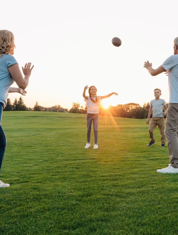 happy grandparents playing american football with grandchildren in park