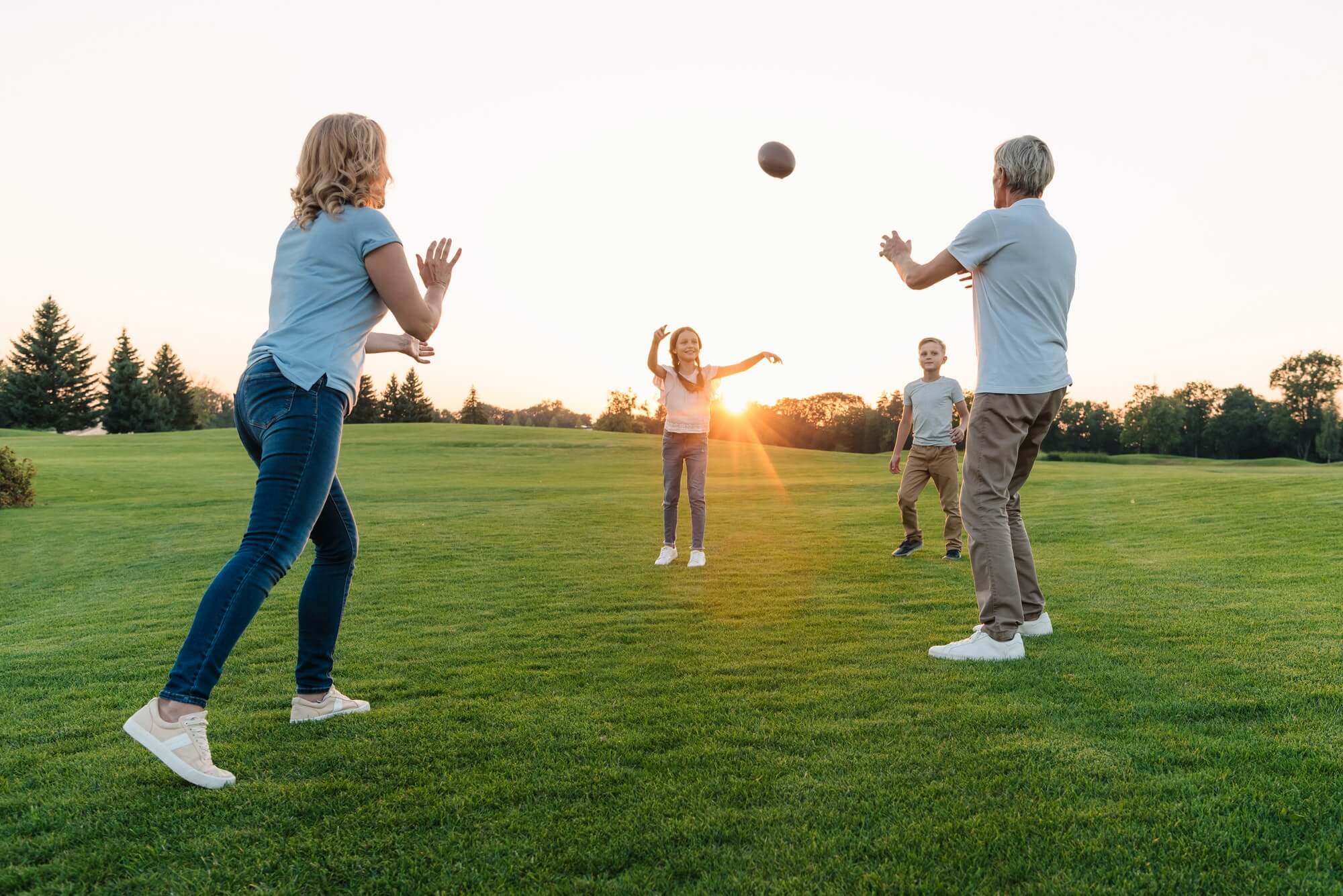 happy grandparents playing american football with grandchildren in park