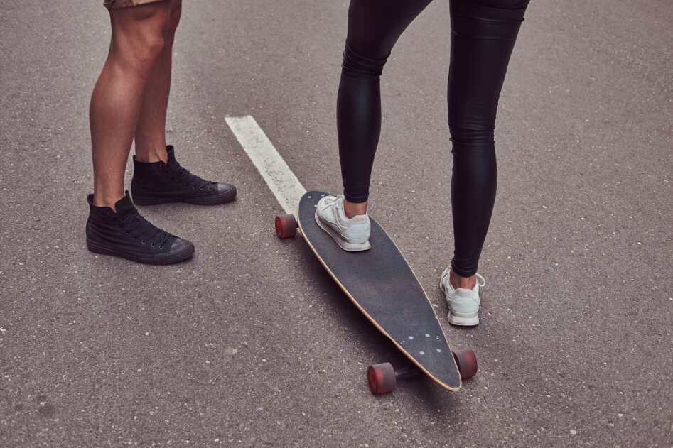 Leisure and sports concept - close-up of teenage couple feet with a longboard on a street.